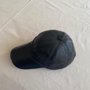 May include: A black leather baseball cap with a stitched design. The cap has a button on the top.