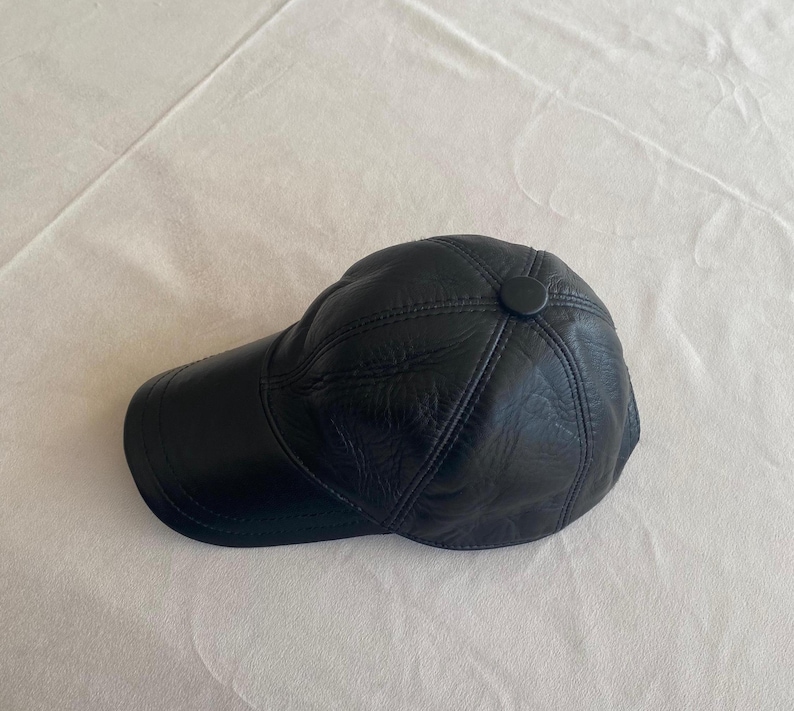 May include: A black leather baseball cap with a stitched design. The cap has a button on the top.