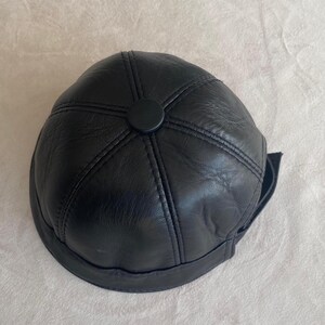 May include: A black leather baseball cap with a stitched design and a black button on top.