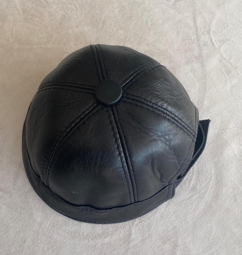 May include: A black leather baseball cap with a stitched design and a black button on top.