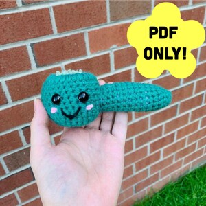 May include: A teal crocheted amigurumi toy shaped like a pipe with a smiling face. The toy has black eyes, pink cheeks, and a black mouth.