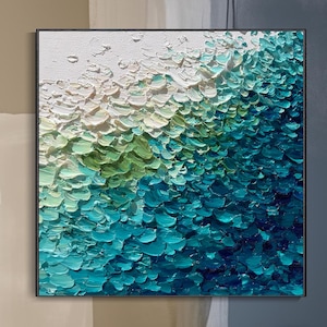May include: Abstract textured wall art in white, green, and blue hues. The artwork uses a layered impasto technique, creating a 3D effect. The painting is framed in black and hangs above a white modern console, adding a contemporary touch.