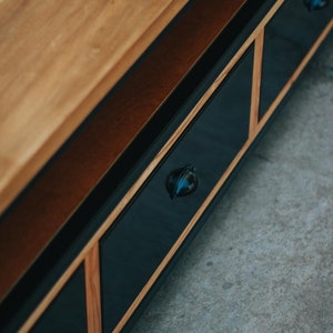 May include: A wooden entertainment unit with three black drawers and black metal knobs. The drawers have a wood trim around the edges.