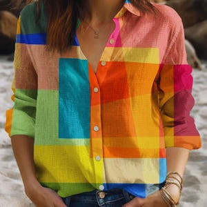 May include: A button-down shirt with a vibrant patchwork design in shades of green, blue, yellow, orange, and pink. The long-sleeved shirt has a collared neckline and white buttons. The shirt is made of a lightweight fabric.