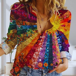 May include: A long-sleeved button-down shirt with a vibrant, rainbow-colored quilted pattern. The design features a spectrum of colors, including red, orange, yellow, green, blue, and purple, with floral and geometric details. The shirt is paired with blue jeans.