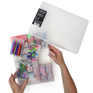 May include: A clear plastic storage box with 18 individual compartments, filled with various craft supplies, including colourful beads, markers, paper clips, and other small items. The box has a clear lid with the text "Craft Pack 18 Box Set" printed on it.