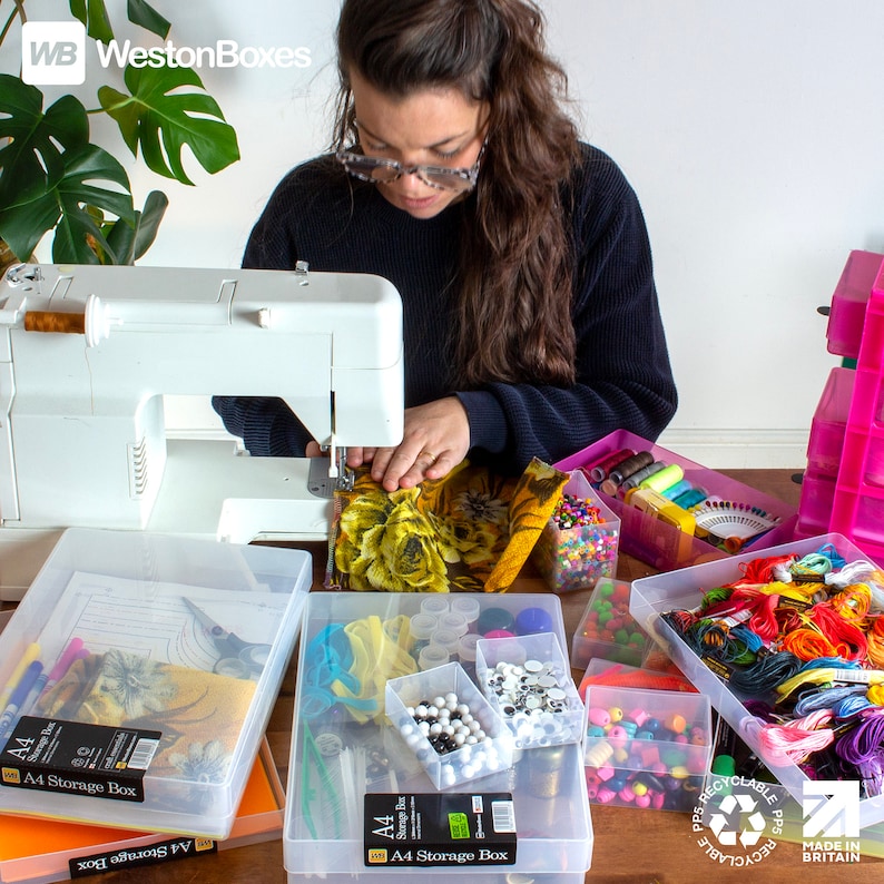 May include: A woman is sewing fabric on a white sewing machine. There are several clear plastic storage boxes filled with colorful craft supplies, including beads, buttons, yarn, and thread. The boxes are labeled "A4 Storage Box".