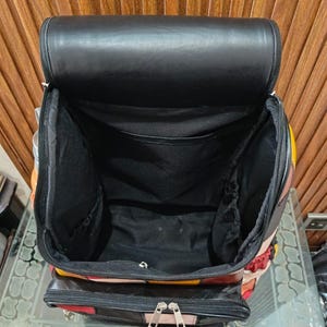 Peut inclure: Sac &agrave; dos noir ouvert avec un int&eacute;rieur spacieux. Le sac pr&eacute;sente un motif patchwork avec des panneaux rouges, jaunes et noirs. Le rabat sup&eacute;rieur est noir et le sac poss&egrave;de une poche avant zipp&eacute;e.