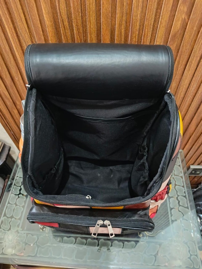 Peut inclure: Sac &agrave; dos noir ouvert avec un int&eacute;rieur spacieux. Le sac pr&eacute;sente un motif patchwork avec des panneaux rouges, jaunes et noirs. Le rabat sup&eacute;rieur est noir et le sac poss&egrave;de une poche avant zipp&eacute;e.