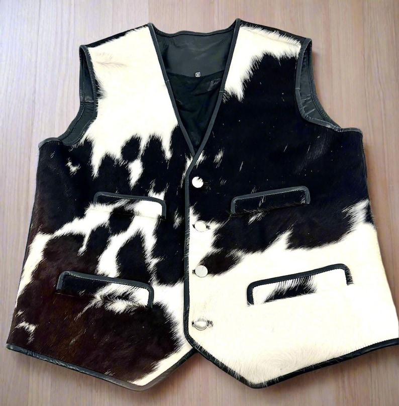 Pu&ograve; includere: Un gilet in pelle di mucca bianco e nero con chiusura a bottone e due tasche su ogni lato. Il gilet ha un bordo in pelle nera.