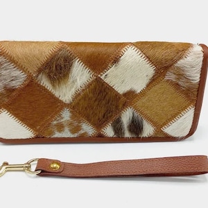Puede incluir: Una cartera de cuero marrón con un diseño de patchwork de diferentes tonos de cuero de vaca marrón y blanco. La cartera tiene un cierre dorado y viene con una correa de cuero marrón a juego.