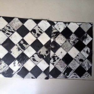 May include: Two black and white cowhide rugs with a checkered pattern. The rugs are made of different sized squares of cowhide, each with a unique pattern of black and white.