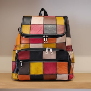 Könnte beinhalten: Ein bunter Patchwork-Rucksack mit einer Reißverschlusstasche vorne. Die Tasche hat eine Vielzahl von Farben, darunter Rot, Gelb, Schwarz und Braun. Der Rucksack hat einen oberen Griff und verstellbare Träger. Abmessungen: ca. 40 cm hoch.
