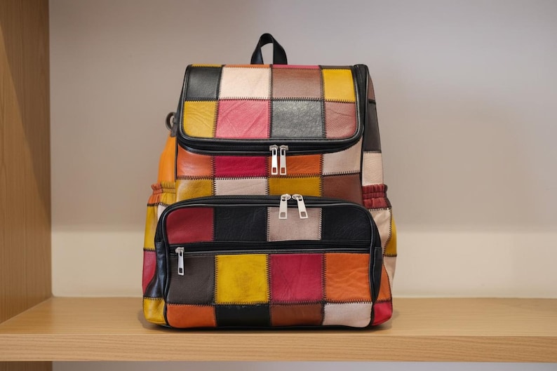 Peut inclure: Sac &agrave; dos patchwork color&eacute; avec une poche avant zipp&eacute;e. Le sac pr&eacute;sente une vari&eacute;t&eacute; de couleurs, notamment le rouge, le jaune, le noir et le marron. Le sac &agrave; dos a une poign&eacute;e sup&eacute;rieure et des bretelles r&eacute;glables. Dimensions : environ 40 cm de haut.