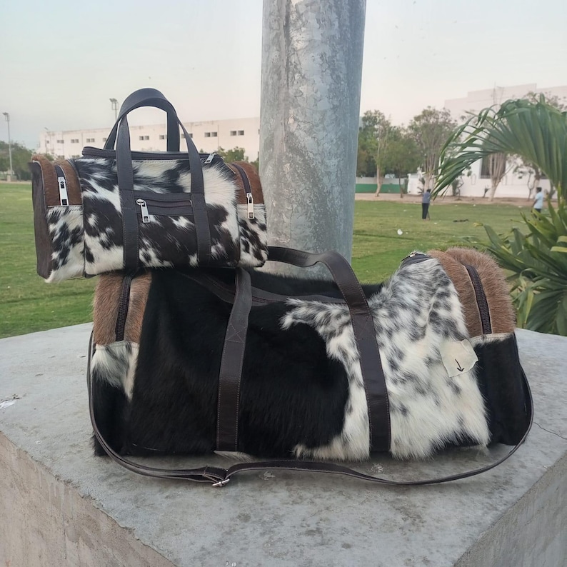 Puede incluir: Dos bolsas de viaje de piel de vaca. La bolsa m&aacute;s grande es negra y blanca con detalles marrones y una correa para el hombro. La bolsa m&aacute;s peque&ntilde;a es negra y blanca con detalles marrones y un asa superior. Ambas bolsas tienen cierre de cremallera.