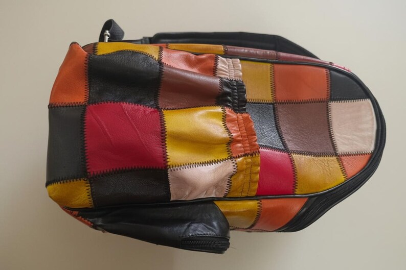 Peut inclure: Un sac patchwork multicolore avec une fermeture &eacute;clair et une poign&eacute;e noires. Le sac pr&eacute;sente une vari&eacute;t&eacute; de couleurs, dont le rouge, le jaune, l'orange, le marron et le noir. Le sac est en cuir et pr&eacute;sente un design g&eacute;om&eacute;trique unique.