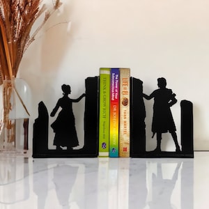 May include: Black metal bookends featuring silhouettes of a woman and a man. The bookends are holding up four books with titles including "Think & Grow Rich" and "Life of Pi".