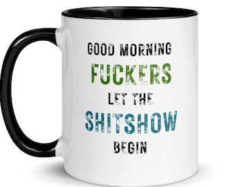 Może przedstawiać: Biały ceramiczny kubek do kawy z czarnym rantem i uchwytem. Kubek ma czarny i zielony wzór z tekstem "Good Morning Fuckers Let The Shitshow Begin".