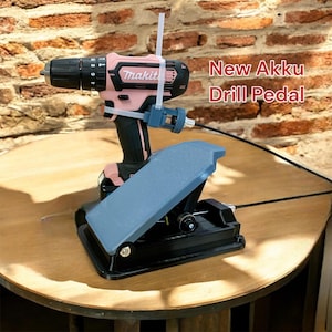 Könnte beinhalten: Ein rosa-schwarzer Akku-Bohrer, der mit einem Kabel an einem schwarzen Fußpedal befestigt ist. Der Bohrer ist mit "Makita" beschriftet. Das Pedal ist mit "New Akku Drill Pedal" beschriftet.