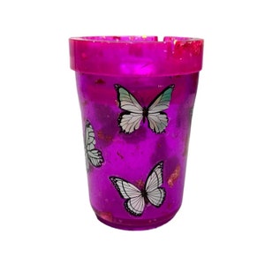May include: A purple glass ashtray with a glittery finish and a design of white butterflies.