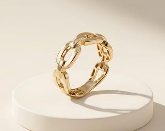 May include: A polished gold ring featuring a continuous chain link design. The band is composed of interconnected oval-shaped metal links with a smooth, reflective surface, creating a uniform and repeating pattern around the entire circumference.