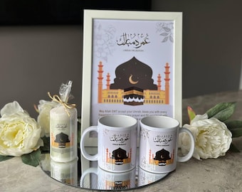 May include: A white framed print with an illustration of a mosque and the text "عمر د مبارك" in Arabic. Two white mugs with the same Arabic text and an illustration of a mosque. A white candle with the same Arabic text and an illustration of a mosque.