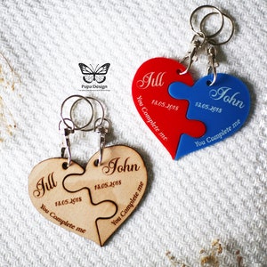 May include: Two wooden heart-shaped puzzle pieces with the names Jill and John, the date 18.05.2018, and the text "You Complete Me". The pieces are attached to a silver key ring.