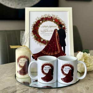 May include: A framed print, two mugs, and a candle are displayed on a mirrored tray. The print shows a couple in traditional dress inside a floral wreath. The mugs and candle share a similar design. The items are likely wedding-themed.