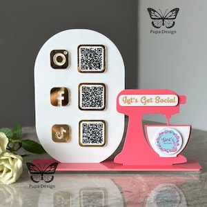 Op de afbeelding: Een witte standaard met een roze mixer en gouden social media-iconen en QR-codes. De mixer heeft de tekst "Let's Get Social" en een logo met de tekst "Gol's Kitchen".