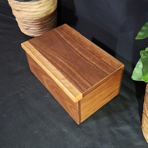 May include: A rectangular wooden box featuring a dark brown lid with a lighter brown wood grain border. The sides of the box are constructed from medium-toned brown wood, showcasing natural wood grain patterns and a smooth, polished finish.