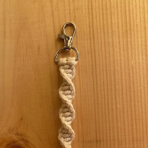 Peut inclure: Un porte-clés en macramé beige avec un fermoir en métal argenté.