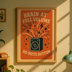 Könnte beinhalten: Ein gerahmtes Poster mit dem Text "BRAIN AT FULL VOLUME NO MUTE BUTTON". Das Poster zeigt ein Retro-Design mit einem Lautsprecher, Noten, Sternen und Blitzen auf orangefarbenem Hintergrund. Der Rahmen ist hellbraun.