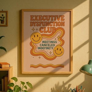 May include: A wooden desk with a framed poster reading "EXECUTIVE DYSFUNCTION CLUB" above it. The desk is covered in books, papers, and stationery. A green desk lamp and a mug of coffee are also present.