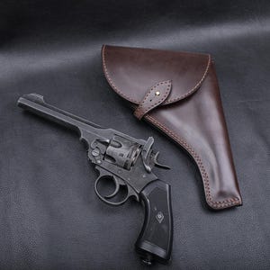 May include: A vintage revolver with a black grip and a brown leather holster. The revolver is dark gray and has a long barrel. The holster is a rich brown color and has a flap closure.