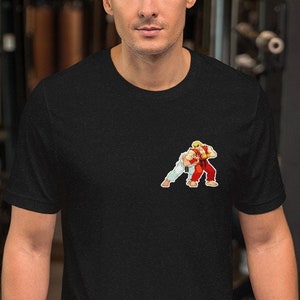 Puede incluir: Una camiseta negra de manga corta con un gráfico de dos personajes de videojuegos luchando. Los personajes están en una pose de lucha, uno en rojo y otro en blanco.