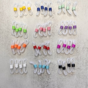 May include: Assortment of clear plastic eyeglass strap holders with colourful bands. The bands are in various colours, including yellow, blue, green, pink, orange, purple, white, turquoise, and black.