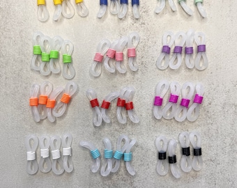 May include: Assortment of clear plastic eyeglass strap holders with colorful bands. The bands are in various colors, including yellow, blue, green, pink, orange, purple, white, turquoise, and black.