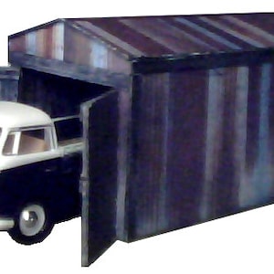 Puede incluir: Una furgoneta vintage blanca y negra con techo blanco está parcialmente dentro de un garaje de metal corrugado de color azul oscuro y gris. Las puertas del garaje están abiertas.