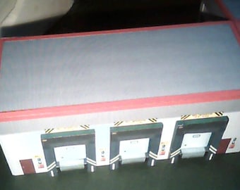 May include: A white building with three loading docks. Each dock has a black and yellow striped safety barrier and a black door. The building has a red roof.