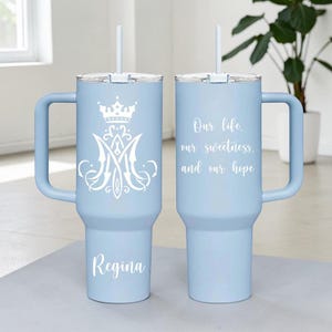 Op de afbeelding: Twee lichtblauwe ge&iuml;soleerde bekers met handvatten en rietjes. E&eacute;n beker heeft een wit kroon- en monogramontwerp met de naam "Regina". De andere heeft de tekst "Our life, our sweetness, and our hope."