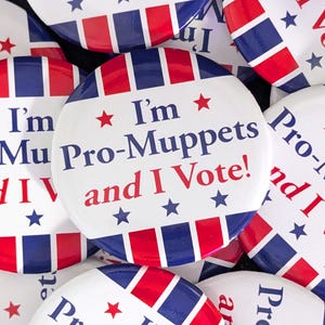 Op de afbeelding: Een verzameling ronde campagnebuttons in rood, wit en blauw. Elke button toont de tekst "I'm Pro-Muppets and I Vote!" in een patriottisch ontwerp met sterren en strepen.