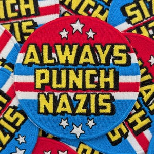 May include: Round embroidered patches with the text "ALWAYS PUNCH NAZIS" in yellow block letters. The patches feature a red background, blue and white stripes, and white stars. The patches have a patriotic design.