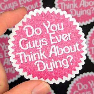 K&ouml;nnte beinhalten: Runder rosa Aufkleber mit einem wei&szlig;en Sternendesign und dem Text "Do You Guys Ever Think About Dying?" in wei&szlig;en Buchstaben.