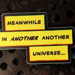 Puede incluir: Pegatina amarilla con texto negro que dice "MEANWHILE IN ANOTHER ANOTHER UNIVERSE..."