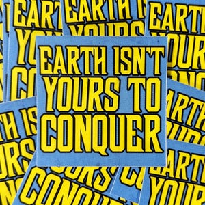Op de afbeelding: Een stapel blauwe en gele stickers met de tekst "Earth Isn't Yours To Conquer".