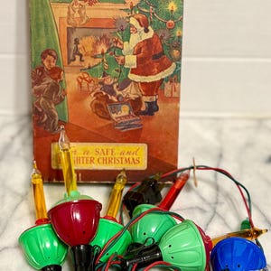 Op de afbeelding: Vintage kerstverlichting van NOMA met een doos met een feestelijke illustratie van de kerstman en een kerstboom. De lampen hebben rode, groene en blauwe lampen met een rood-groene draad.