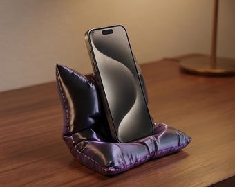 Suporte/apoio para celular exclusivo, impresso em 3D, em formato de "almofada fofa", nas cores roxo e preto.