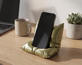 Suporte/base para celular exclusivo com impressão 3D em formato de "almofada fofa" nas cores dourado e prateado.