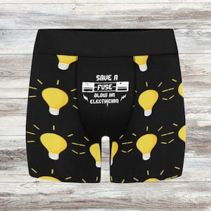 May include: Black boxer briefs with a repeating pattern of yellow light bulbs with white bases and radiating lines. The waistband is black. The front of the briefs has the text "SAVE A FUSE BLOW AN ELECTRICIAN" in white.