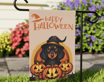 May include: A Halloween garden flag with a black and brown dachshund wearing a witch's hat and holding three pumpkins. The flag has a peach background with the text "Happy Halloween" in black.